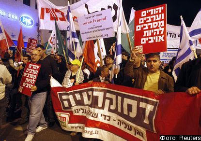 Left wing protestors hold posters and banners as they march in the streets of Tel Aviv