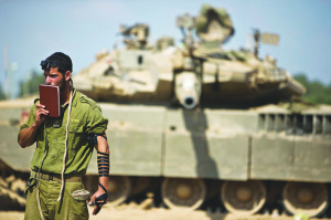 An Israeli soldier prays in front of a tank at a staging area near the border with the Gaza Strip