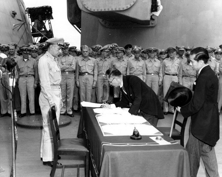 Министр внутренних дел Японии Мамору Сигэмицу подписывает Акт о капитуляции Японии на борту USS Миссури, под наблюдением генерала  Ричарда К. Сазерленда, 2 сентября 1945