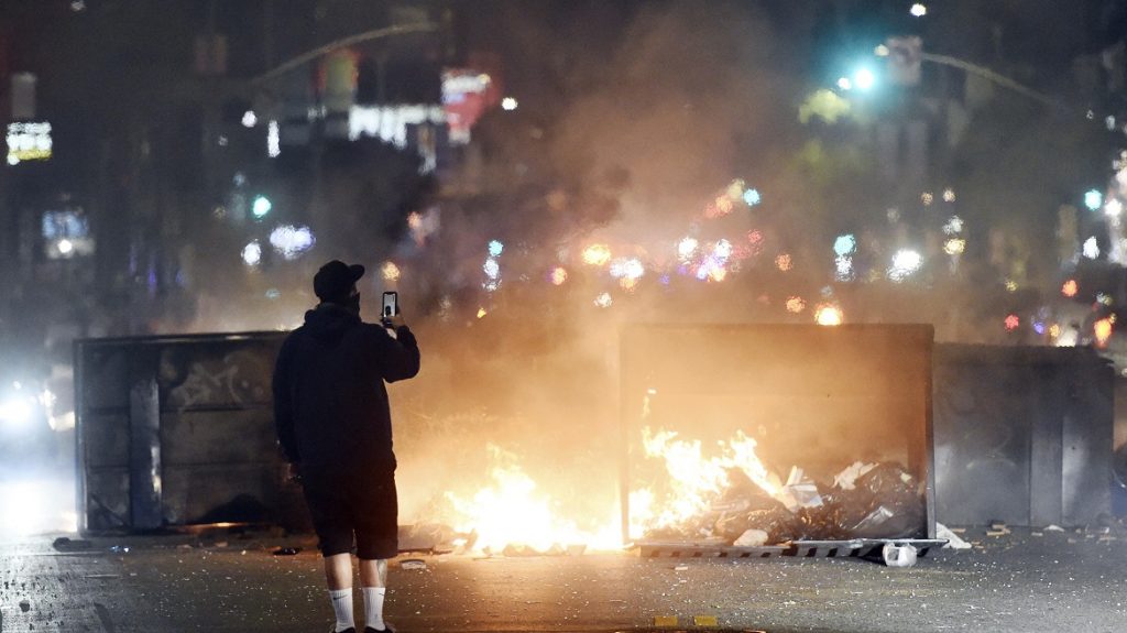 A man films himself in front of a fire in the middle of Melrose Avenue, Saturday, May 30, 2020, in Los Angeles. Protests were held in U.S. cities over the death of George Floyd, a black man who died after being restrained by Minneapolis police officers on May 25. (AP Photo/Chris Pizzello)