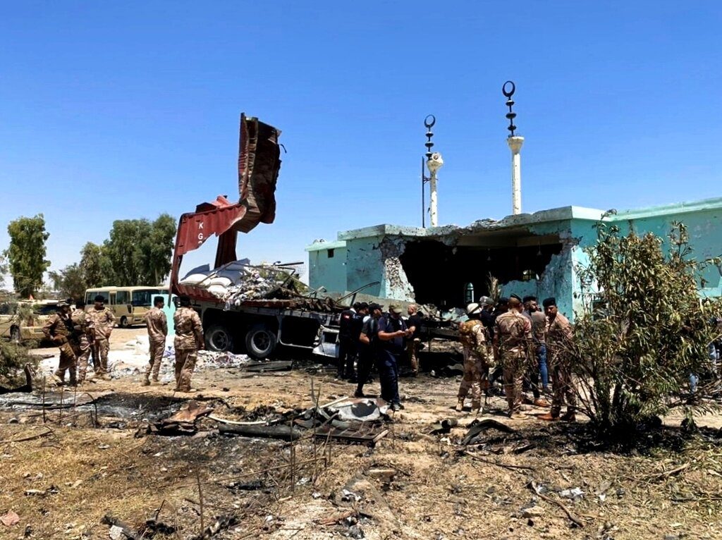 Security forces gather near a destroyed truck used as rocket launcher that sits near a damaged mosque in Anbar, Iraq, Thursday, July 8, 2021. Rockets targeted the heavily fortified Green Zone in the Iraqi capital Baghdad on Thursday, causing some damage but no reported casualties, Iraqi security forces said. (Joint Operations Command Media Office, via AP)